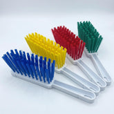 Four plastic cleaning brushes with white handles and colorful bristles in blue, yellow, red, and green, arranged diagonally on a white background.