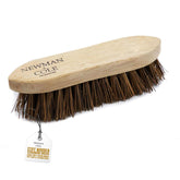 A Newman Cole stiff wooden grooming brush with dark brown bristles and a light natural wood handle, shown with its branded paper tag on a white background.