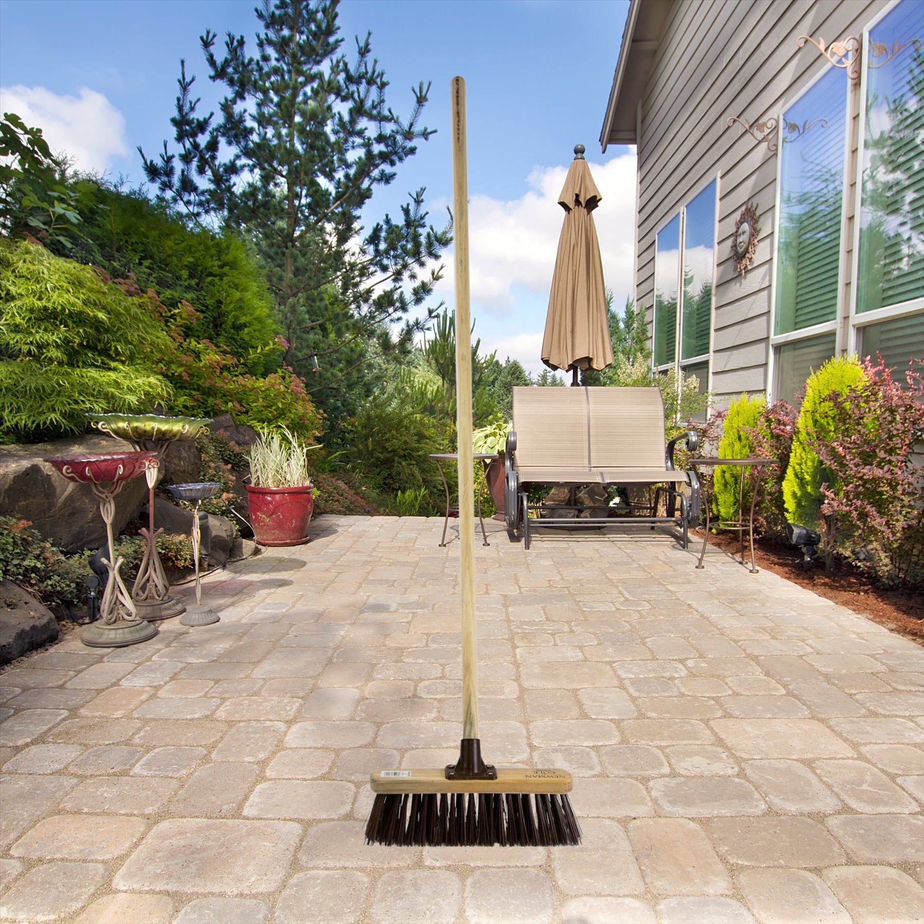 Environmental image of 12" Newman & Cole Stiff PVC Broom with Wooden Handle on a household patio