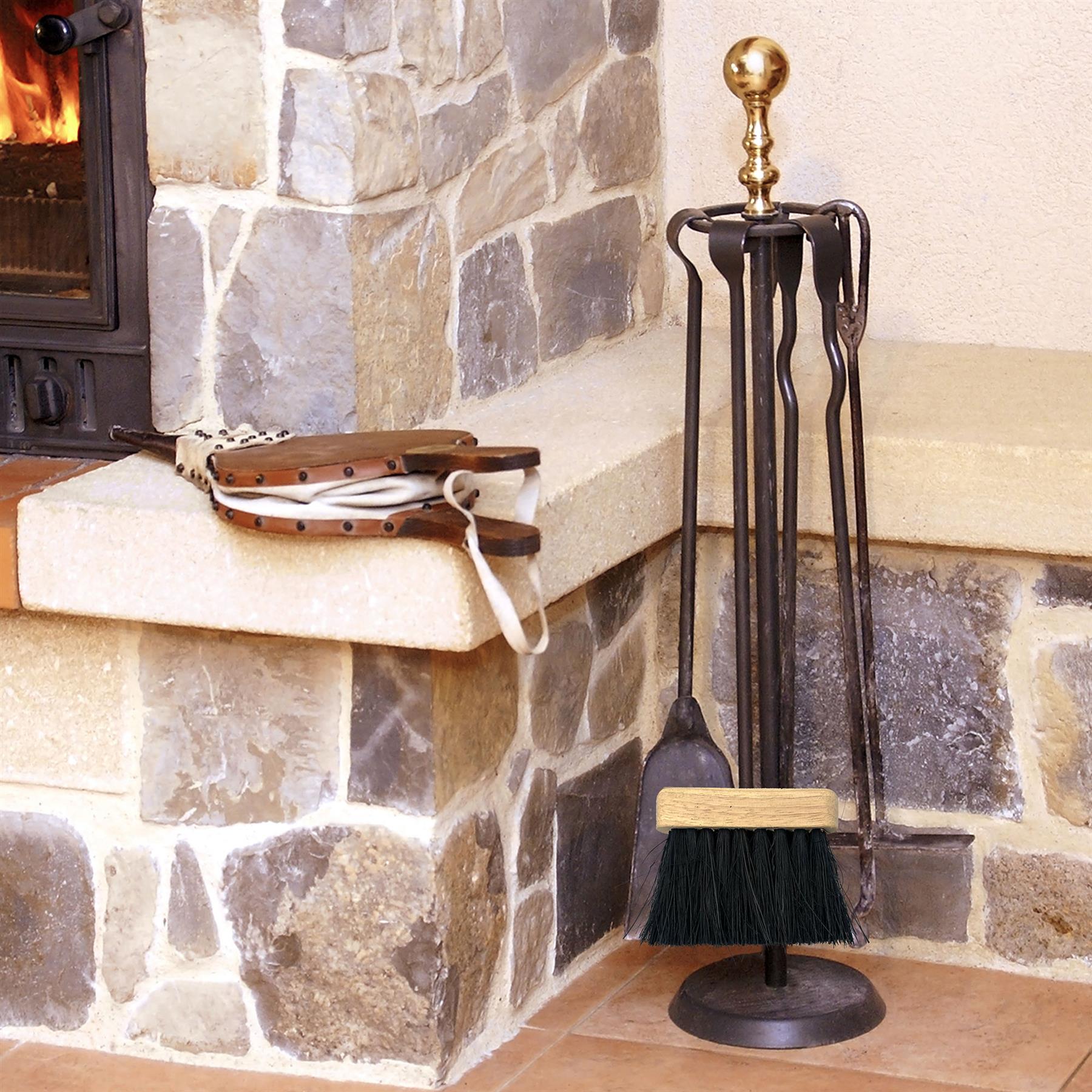 A black wrought-iron fireplace tool set with a brass finial and a light wood handle, displayed on a stand next to a stone fireplace. A leather-wrapped poker is resting on the stone hearth.
