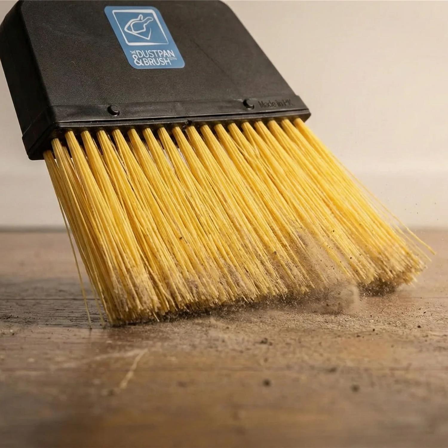 A close up of the Replacement Stiff Brush for Long Handled Dustpan and Brush Set brushing up dust and dirt on a wooden floor
