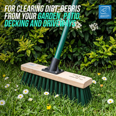 A green garden brush with a light wood handle and dark green bristles is shown in a grassy garden setting with white daisies and leafy green shrubs. Text at the top reads 'FOR CLEARING DIRT, DEBRIS FROM YOUR GARDEN, PATIO, DECKING AND DRIVEWAYS,' and a blue 'MOTION EDITION' logo appears in the top right.