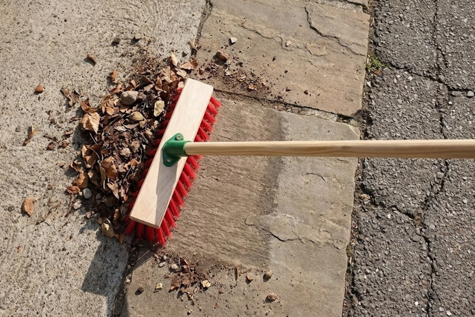 Environmental image of 11.5" Stiff Red PVC Broom Head cleaning outdoor patio and sweeping up leaves 