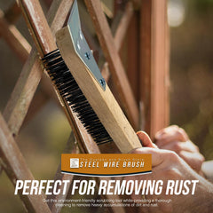 A close-up of a hand holding a wooden-handled steel wire brush against a rusty metal lattice structure, 