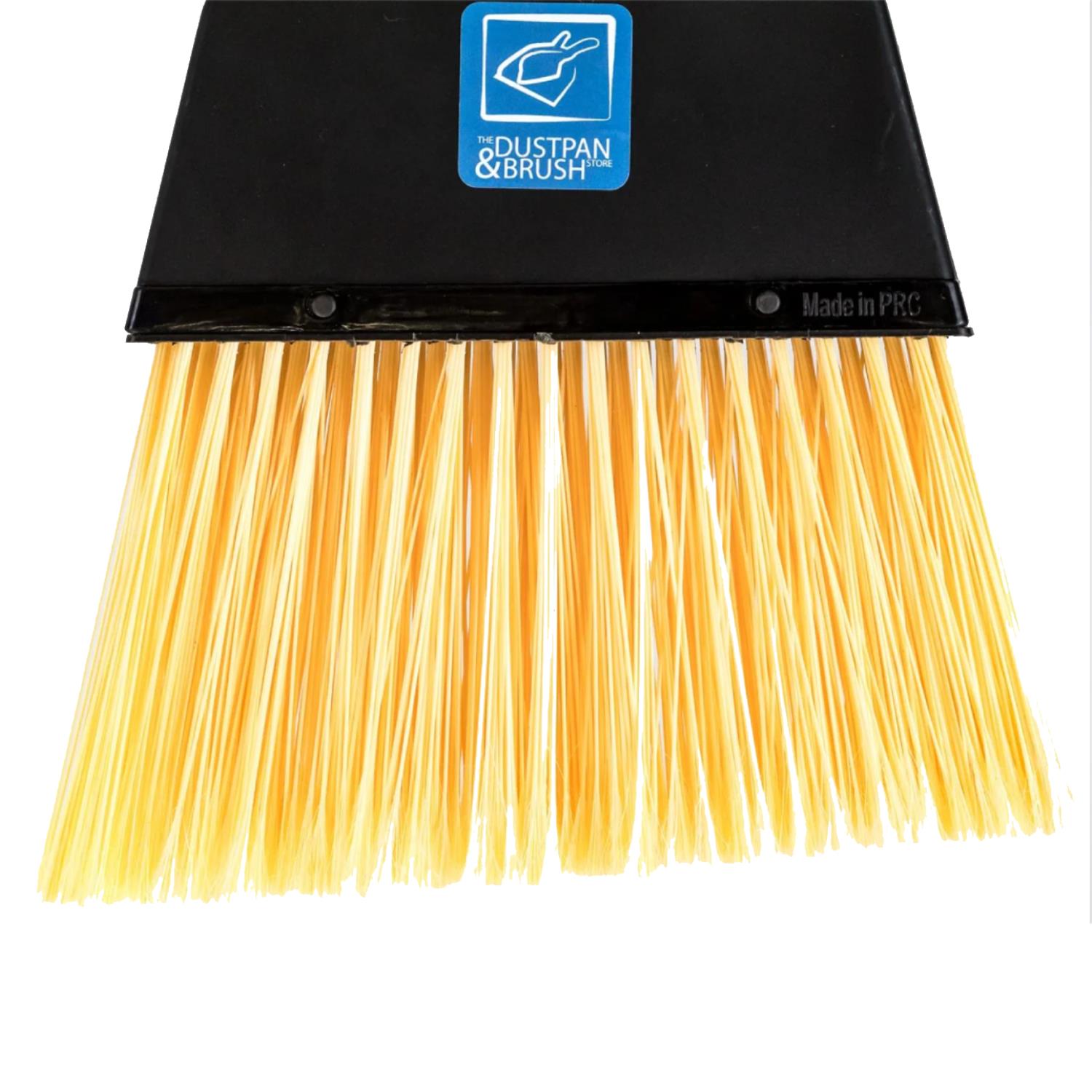 A close-up of the stiff brush broom head with a black plastic frame, a blue DUSTPAN & BRUSH STORE logo sticker, and dense yellow nylon bristles on a white background.