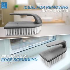 A grey and white cleaning brush shown in two bathroom-use scenarios: on a bathroom counter with text reading 'IDEAL FOR REMOVING BATH STAINS,' and on a window ledge with text reading 'EFFORTLESS EDGE SCRUBBING.' The brush has a dark grey handle and white bristles.