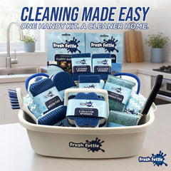 A Fresh Fettle cleaning kit displayed in a white plastic basket on a kitchen counter, with a sink and kitchen background visible. The kit includes blue and white cleaning sponges, scrubbers, mops, and a black brush, with multiple branded packages arranged inside the basket.
